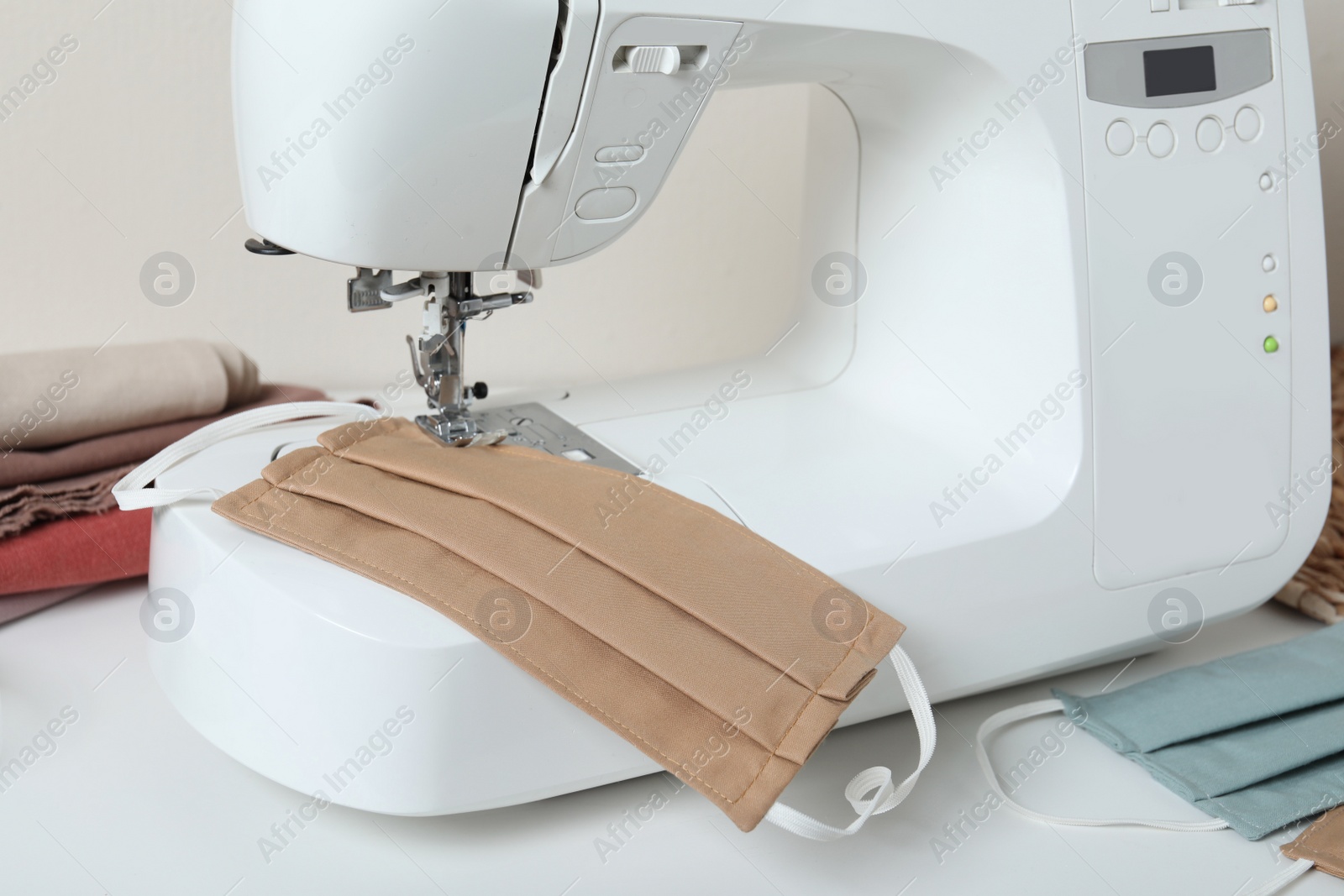 Photo of Sewing machine with homemade protective mask on white table