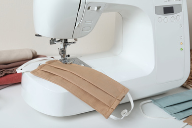 Photo of Sewing machine with homemade protective mask on white table