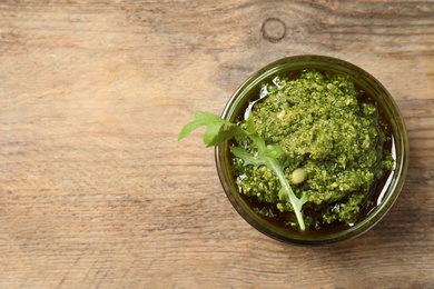 Photo of Bowl of tasty arugula pesto on wooden table, top view. Space for text