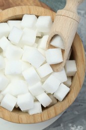 White sugar cubes in wooden bowl and scoop on grey table, top view