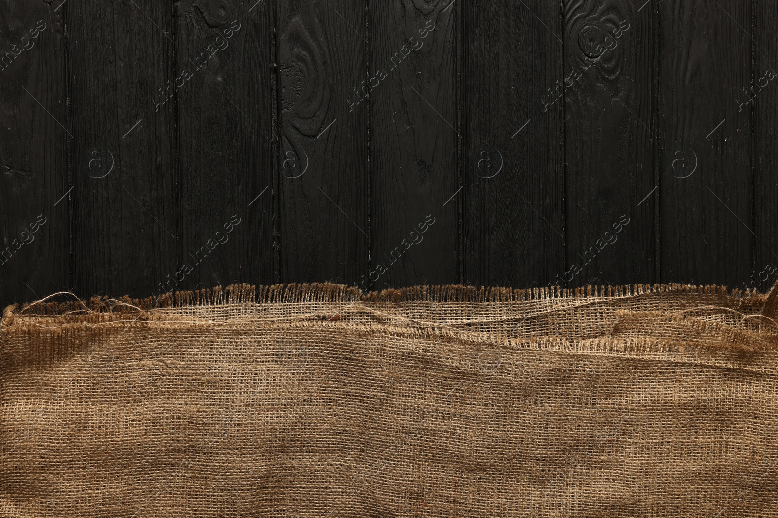 Photo of Burlap fabric on black wooden table, top view. Space for text