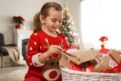 Photo of Cute little girl taking gift from Christmas advent calendar at home