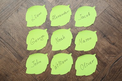 Photo of Paper stickers with different names on wooden background, flat lay. Choosing baby's name