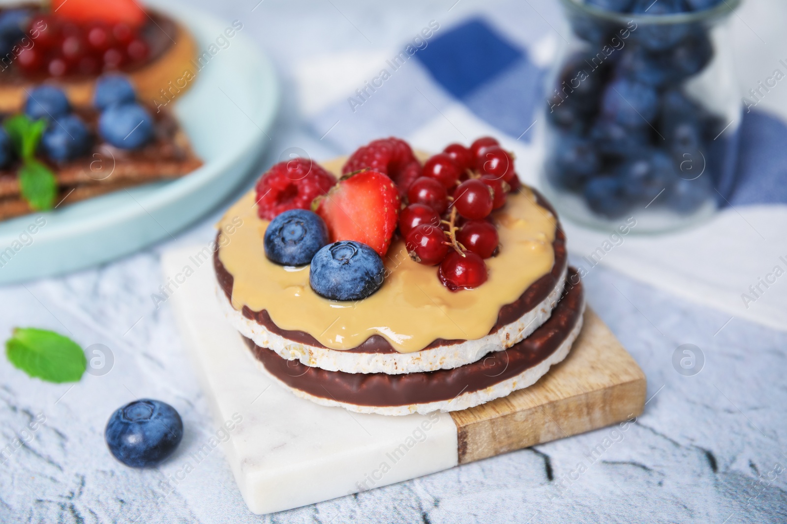 Photo of Crunchy rice cakes with peanut butter and sweet berries on white textured table, closeup