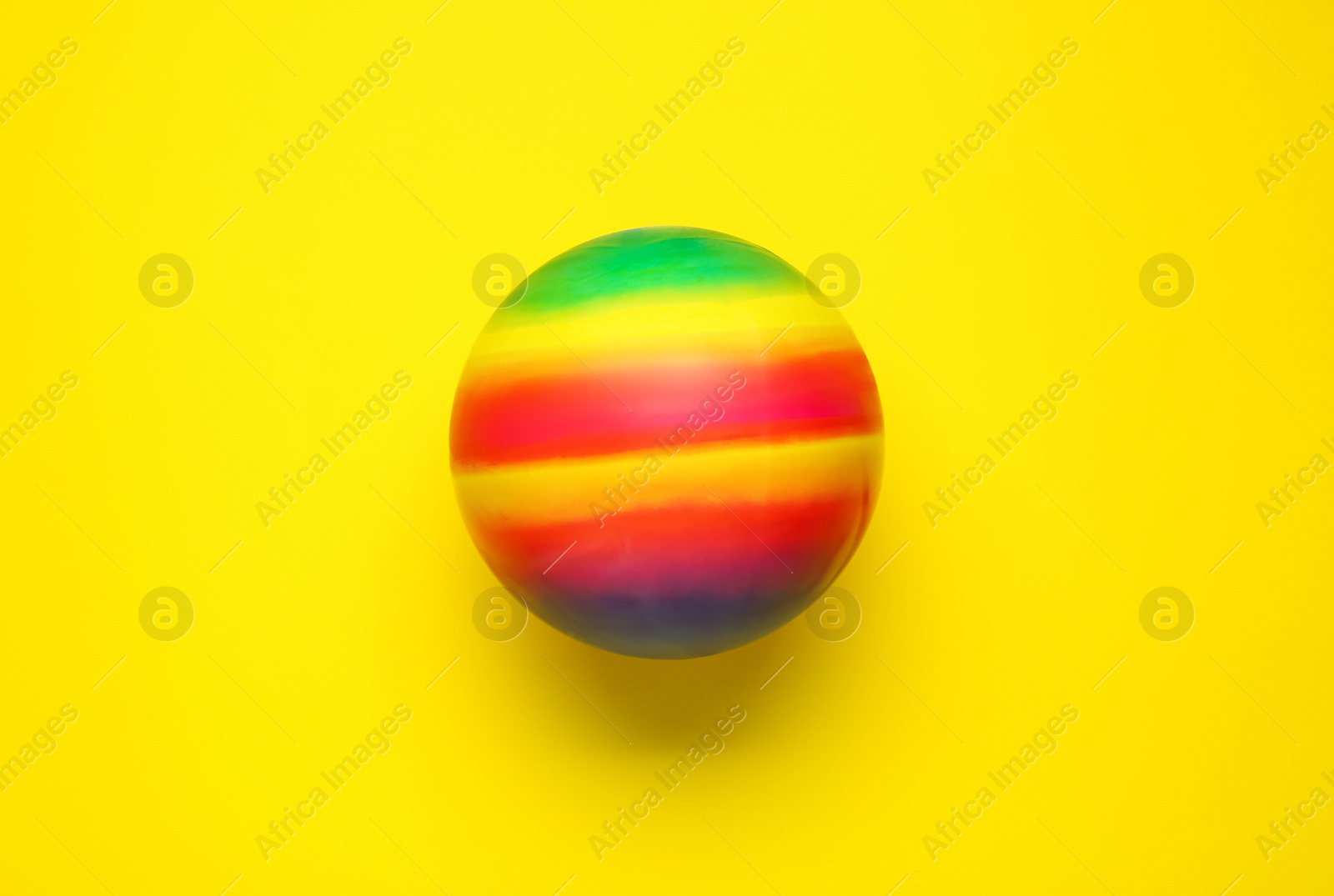 Photo of Bright rubber kids' ball on yellow background, top view