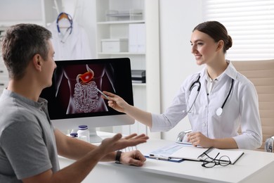 Gastroenterologist showing screen with illustration of digestive tract to patient at table in clinic