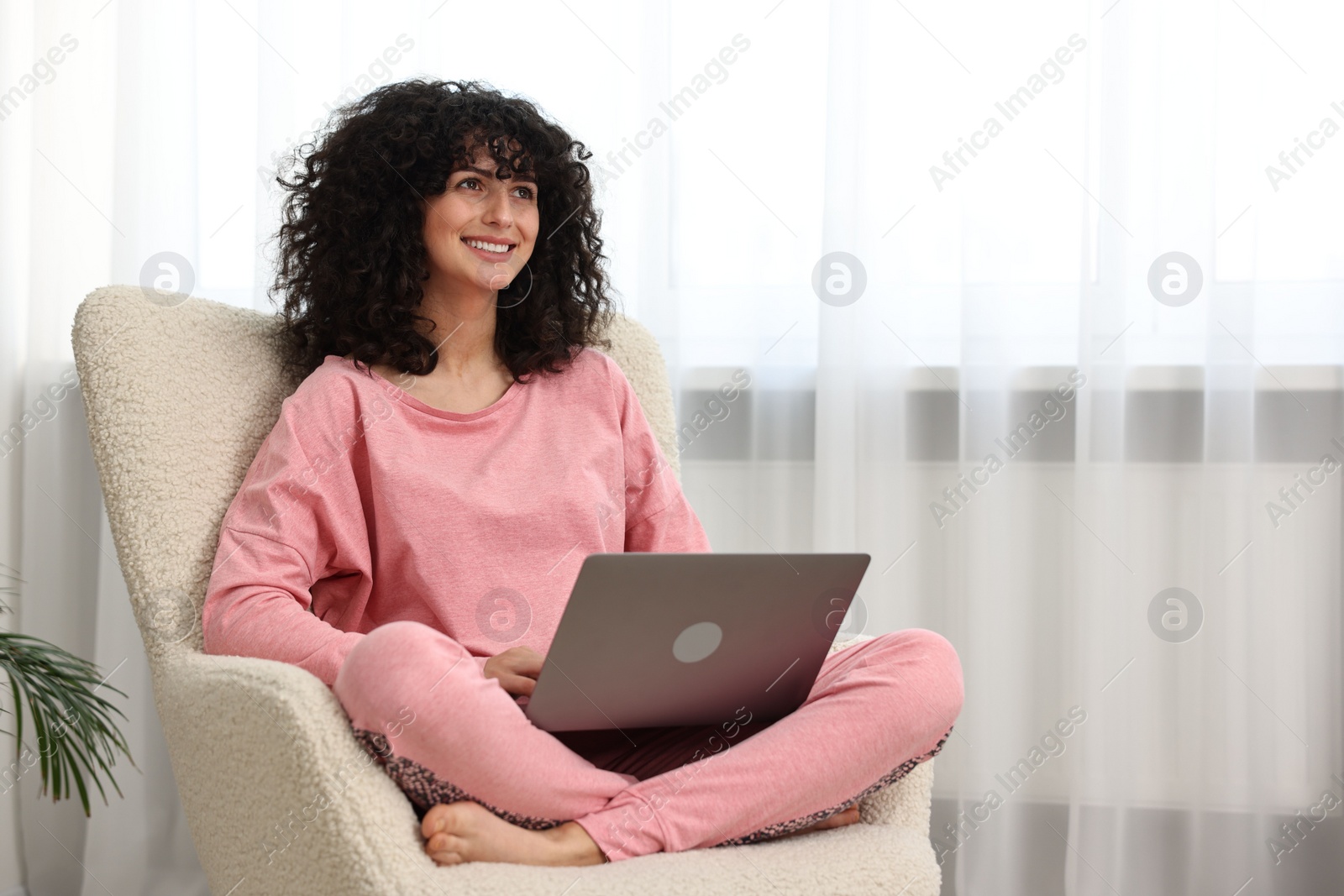 Photo of Beautiful young woman in stylish pyjama with laptop on armchair at home