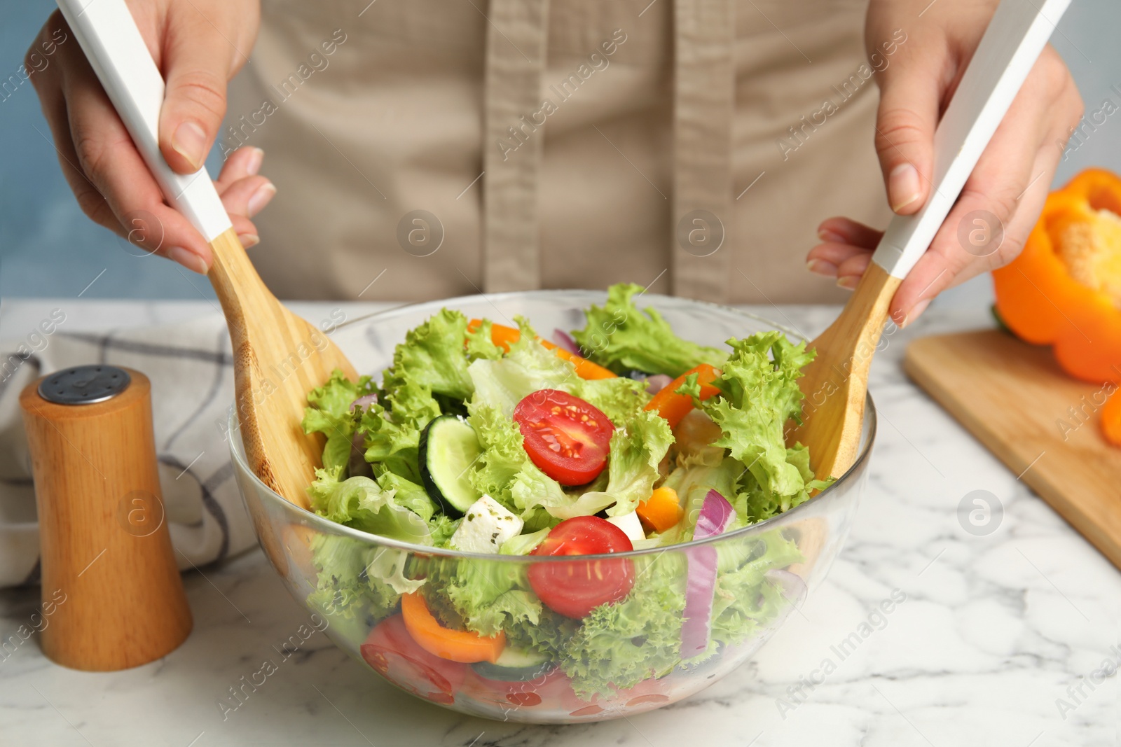 Photo of Woman preparing tasty fresh Greek salad in bowl at white marble table, closeup