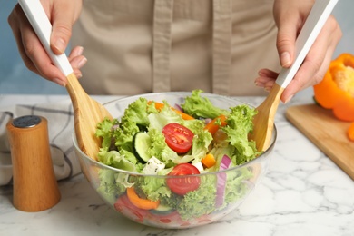 Photo of Woman preparing tasty fresh Greek salad in bowl at white marble table, closeup