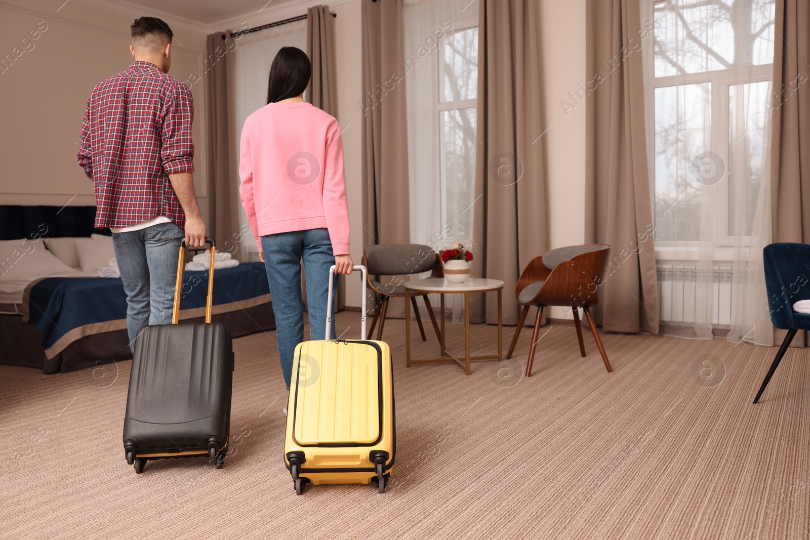 Photo of Couple with suitcases walking into hotel room, back view
