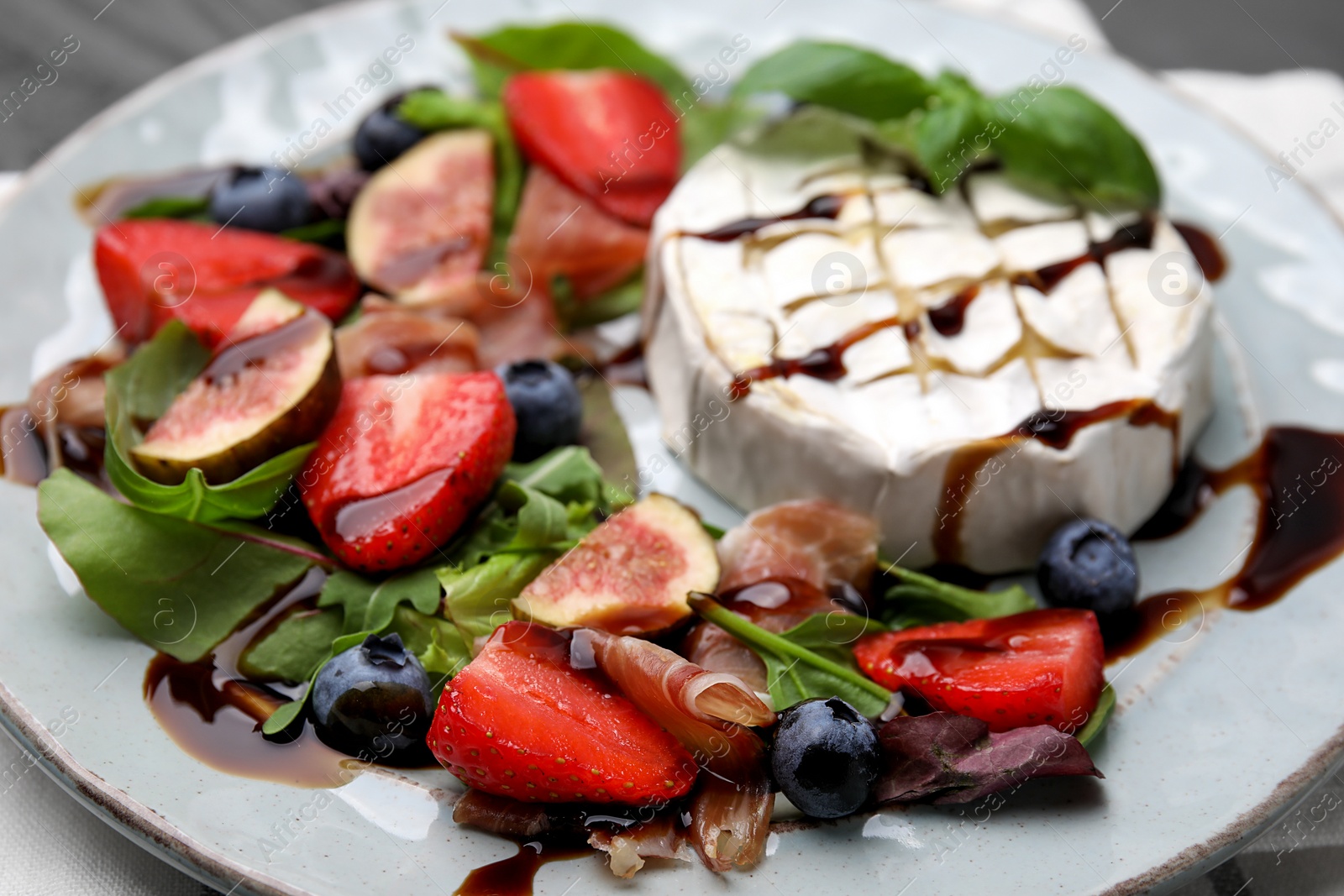 Photo of Delicious salad with brie cheese, prosciutto, berries and balsamic vinegar on plate, closeup