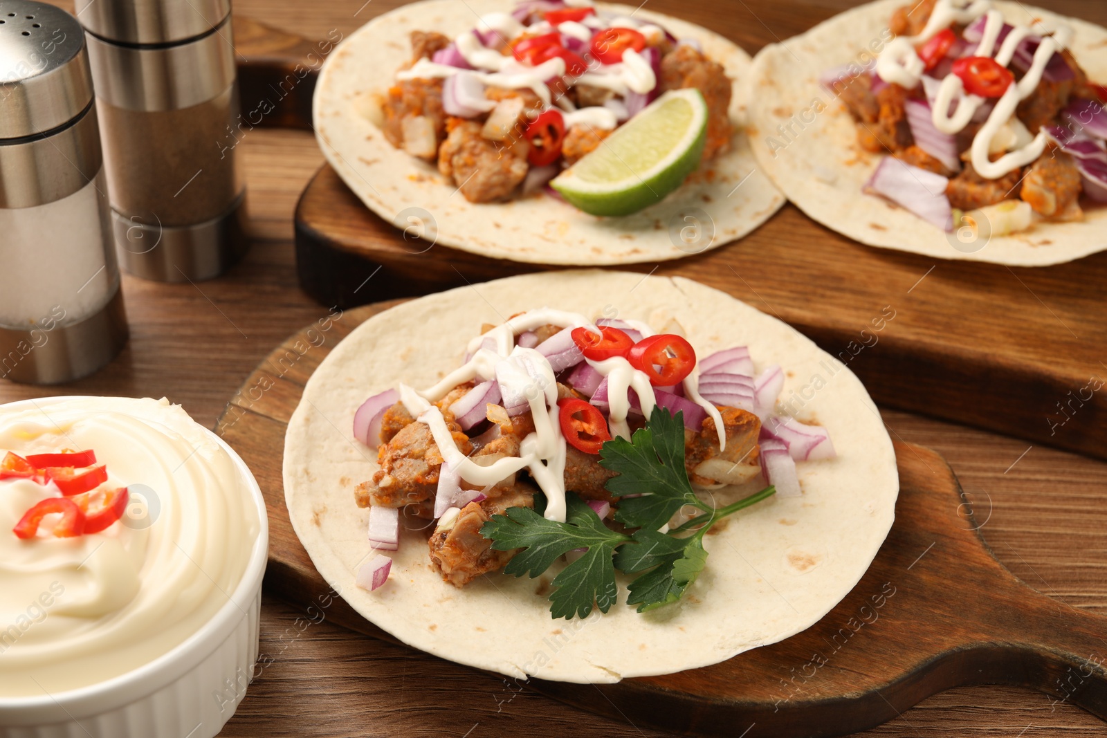 Photo of Delicious tacos with vegetables, meat and sauce on wooden table