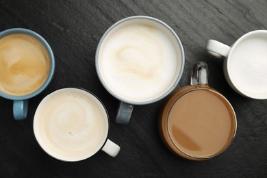 Different coffee drinks in cups on dark textured table, flat lay