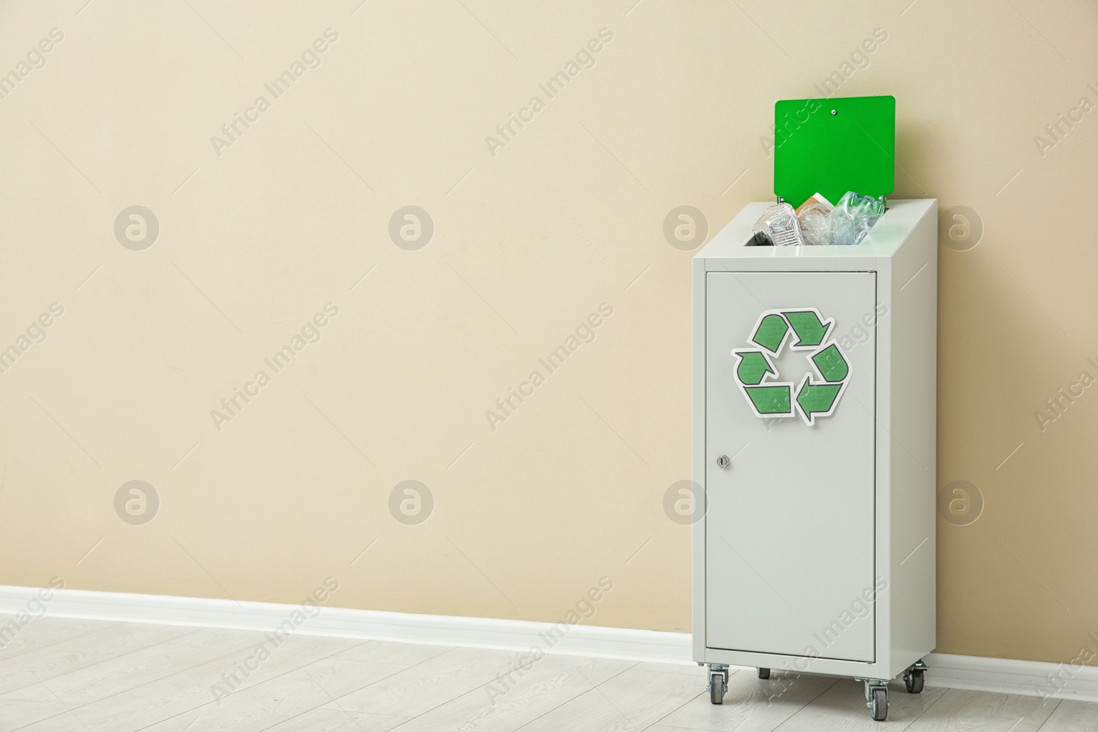 Photo of Trash bin with recycling symbol near color wall indoors. Space for text