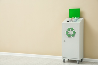 Trash bin with recycling symbol near color wall indoors. Space for text