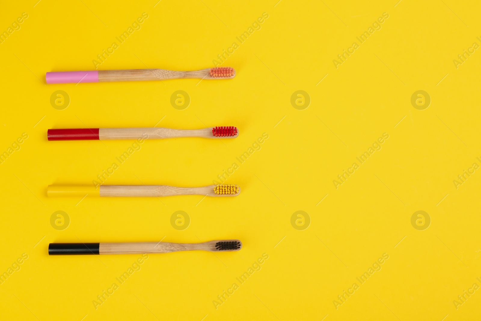 Photo of Toothbrushes made of bamboo on yellow background, flat lay. Space for text