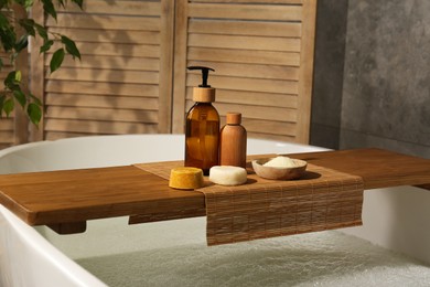 Photo of Wooden tray with spa products on bath tub in bathroom