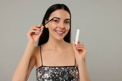 Photo of Beautiful young woman applying mascara on grey background