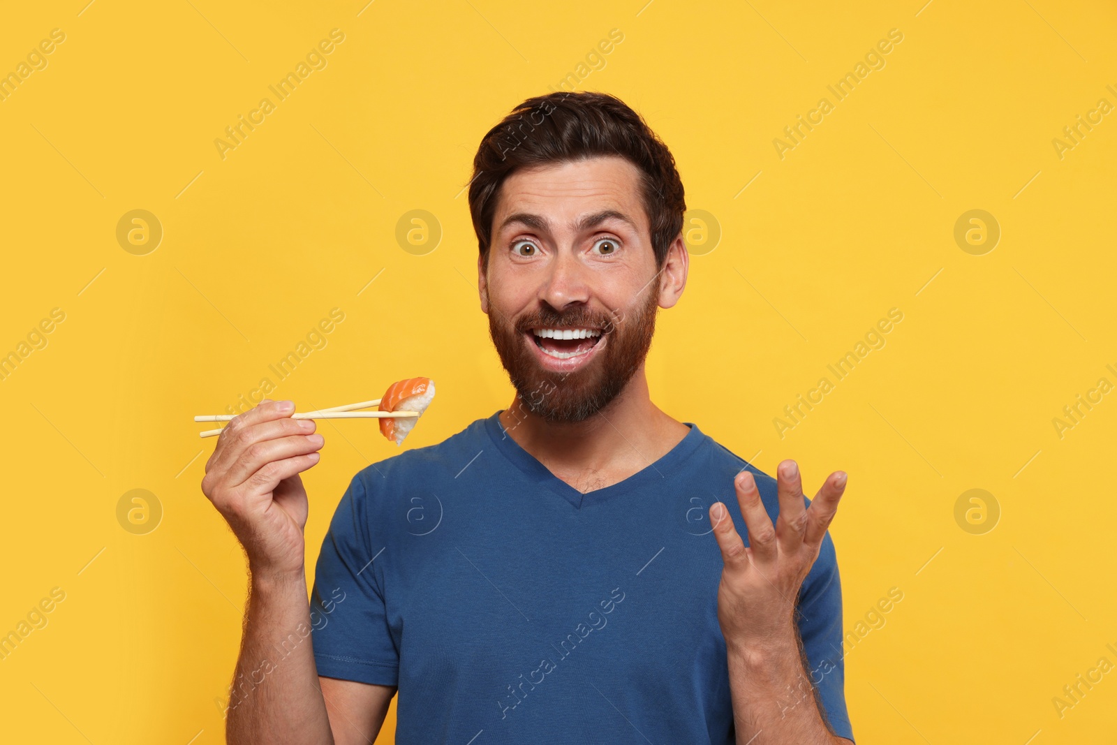 Photo of Emotional man holding sushi with chopsticks on orange background