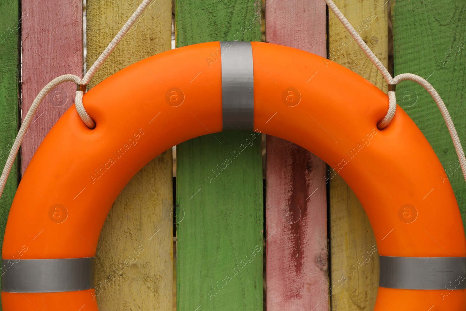 Photo of Orange lifebuoy hanging on color wooden fence, closeup. Rescue equipment