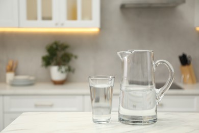 Jug and glass with clear water on white table in kitchen, space for text