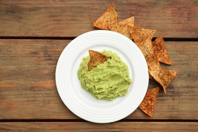 Photo of Delicious guacamole made of avocados and nachos on wooden table, flat lay