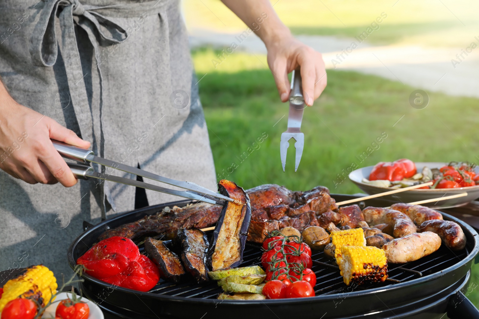 Photo of Man cooking meat and vegetables on barbecue grill in park, closeup