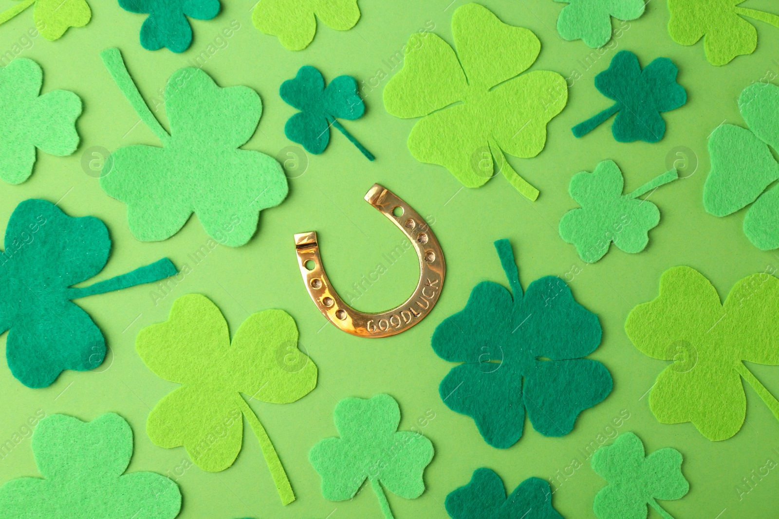 Photo of St. Patrick's day. Golden horseshoe and decorative clover leaves on green background, flat lay