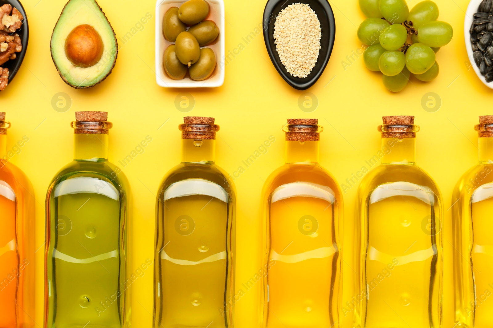 Photo of Vegetable fats. Different oils in glass bottles and ingredients on yellow table, flat lay