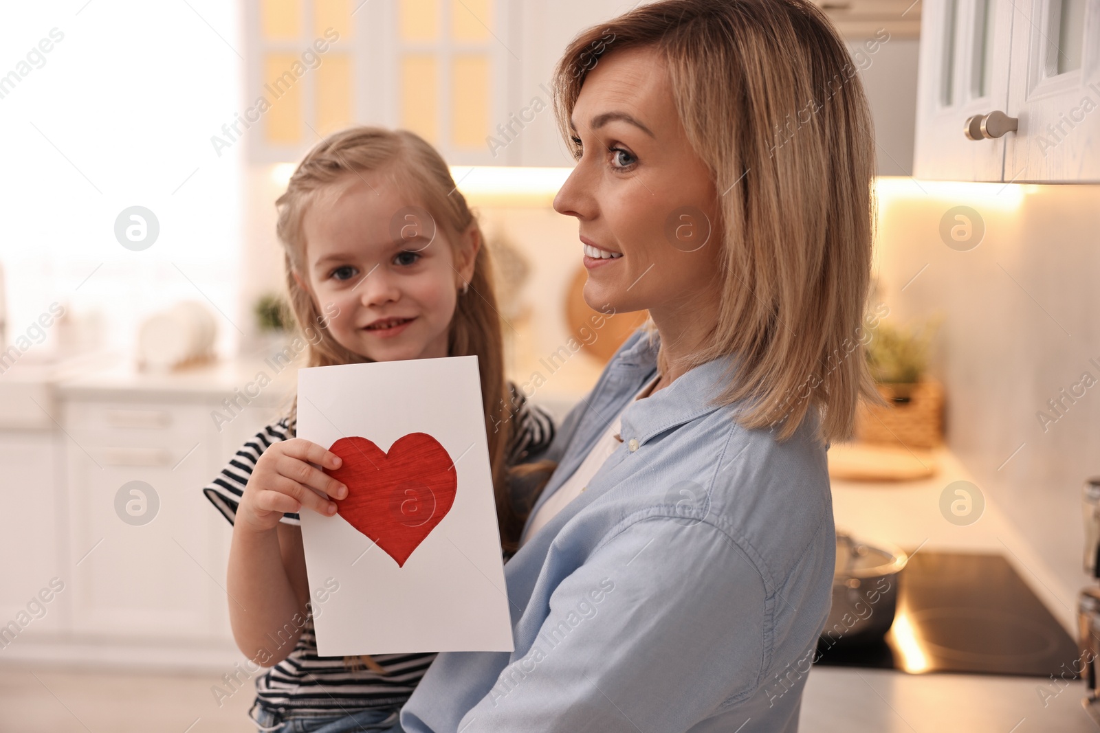 Photo of Little daughter congratulating her mom with greeting card in kitchen. Happy Mother's Day