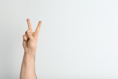 Photo of Young man showing victory gesture on light background. Space for text