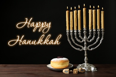 Image of Happy Hanukkah. Silver menorah, sufganiyah and dreidels on wooden table against black background 