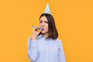 Young woman in party hat with blower on yellow background