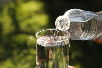 Photo of Pouring fresh water from bottle into glass outdoors, closeup