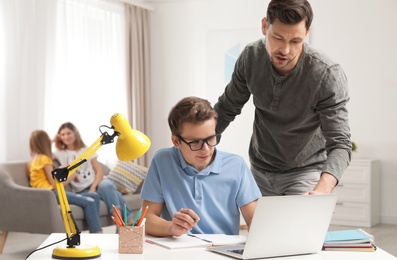 Photo of Father helping his teenager son with homework indoors