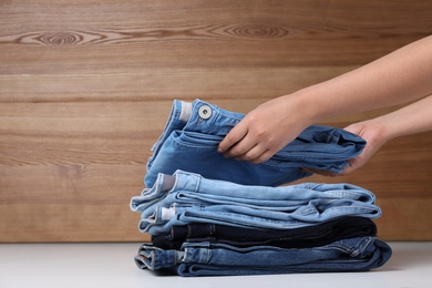 Photo of Young woman folding stylish jeans on table