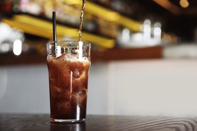 Pouring cola into glass with ice cubes on table indoors. Space for text