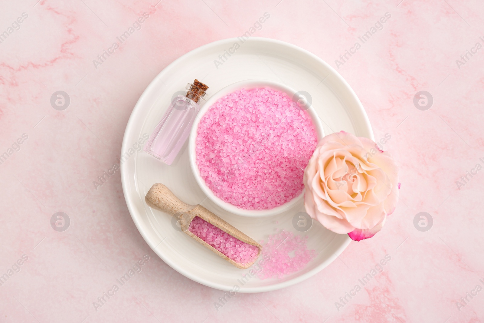 Photo of Bowl and scoop with sea salt, beautiful rose on pink marble table, top view