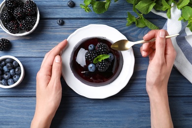 Woman eating delicious fresh jelly at blue wooden table, top view