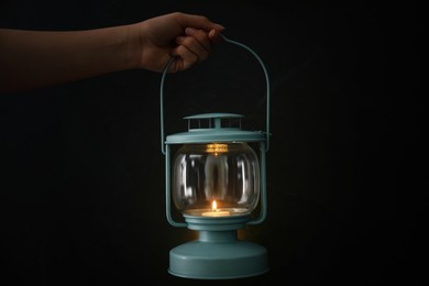 Photo of Woman holding lantern with burning candle on black background, closeup