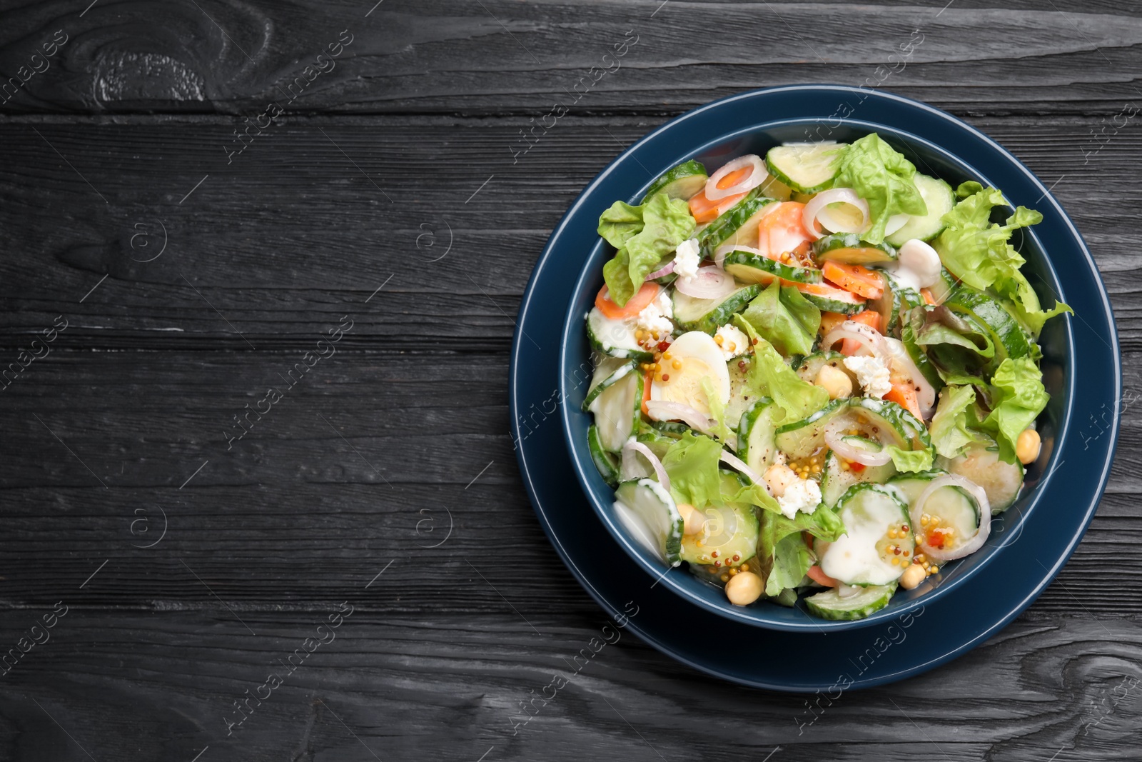 Photo of Bowl of delicious cucumber salad on black wooden table, top view. Space for text