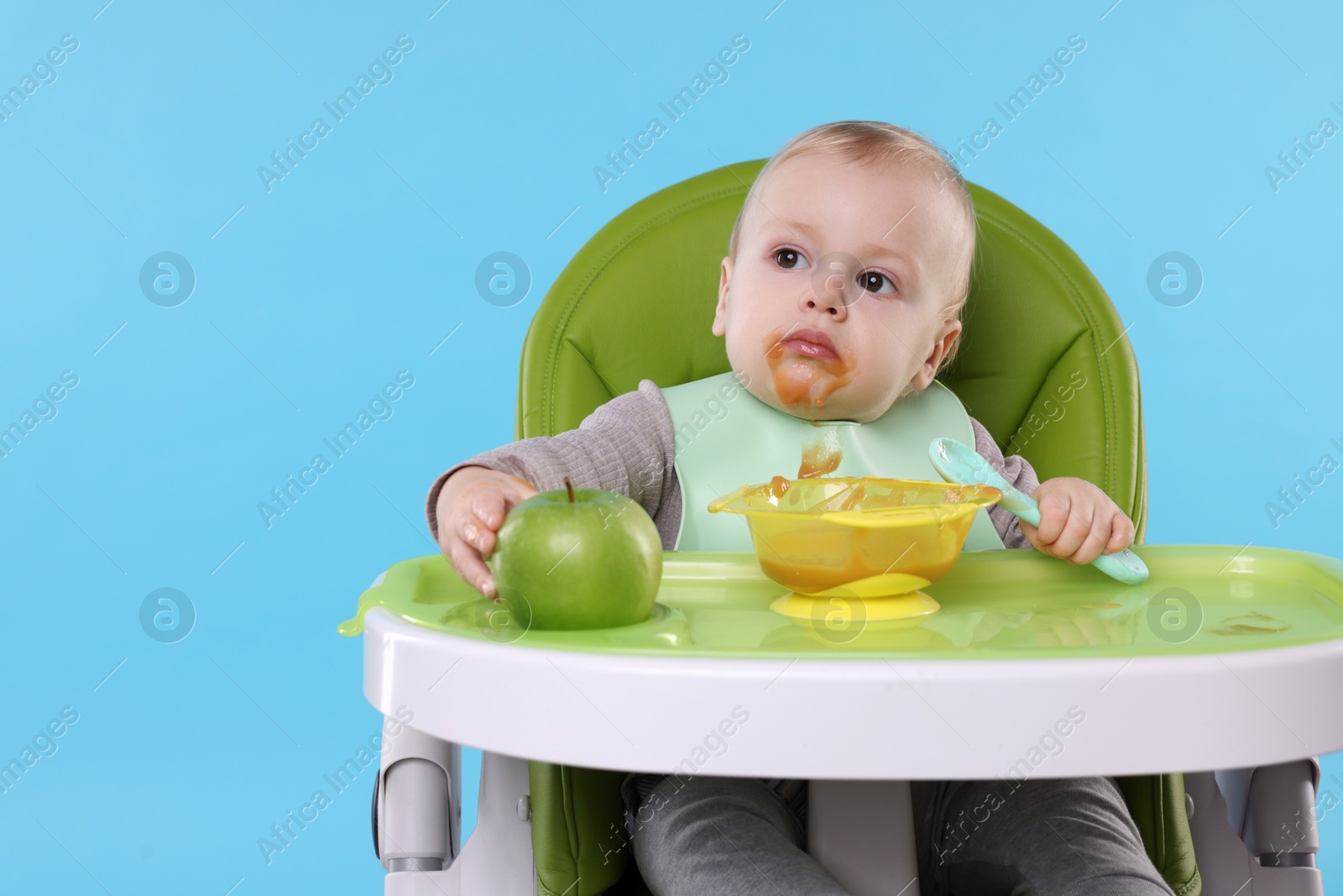 Photo of Cute little baby eating healthy food in high chair on light blue background, space for text