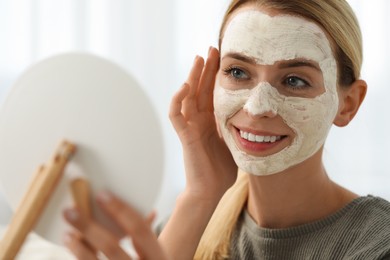 Photo of Young woman with face mask looking into mirror. Spa treatments