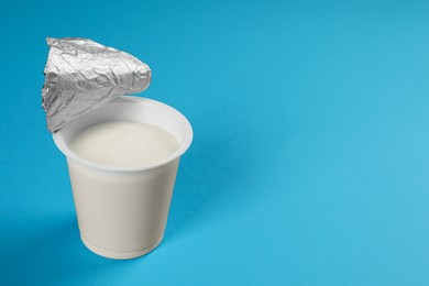 Photo of Plastic cup with tasty yogurt on light blue background, space for text