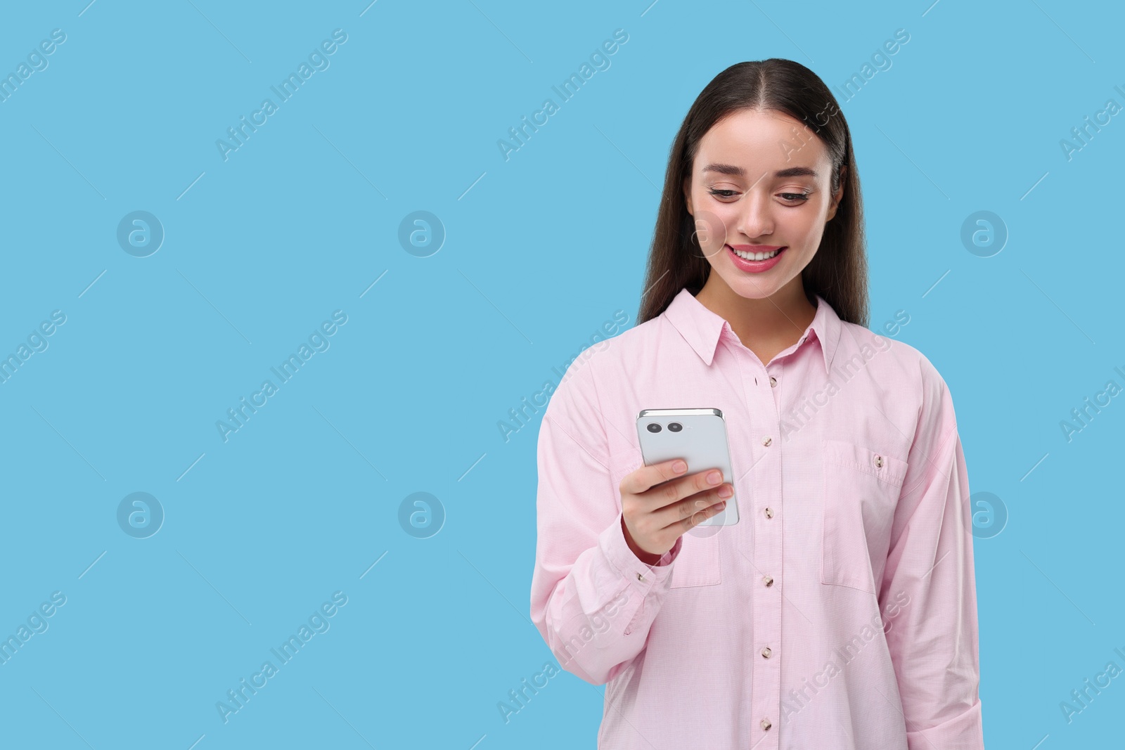 Photo of Happy woman sending message via smartphone on light blue background, space for text