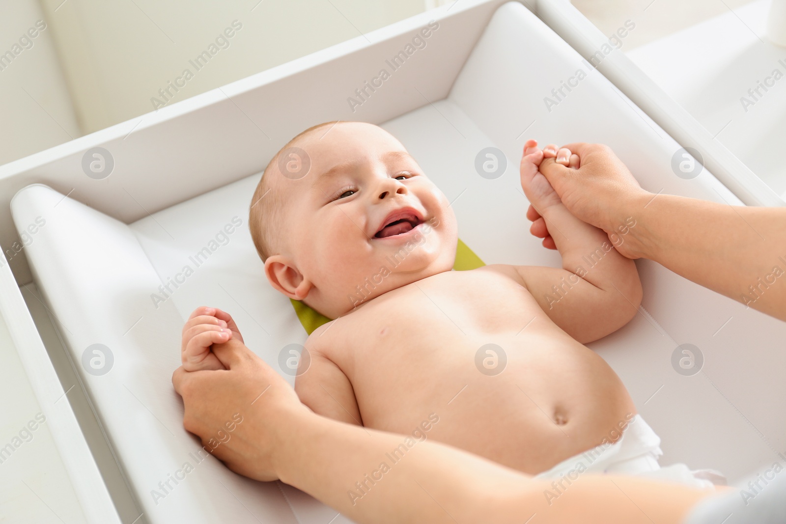 Photo of Young woman massaging cute baby on changing table