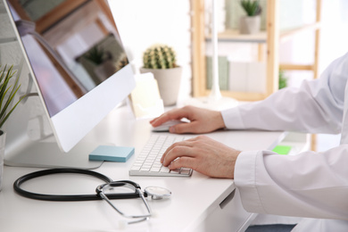 Doctor working with computer at desk in office, closeup
