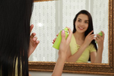 Photo of Woman applying dry shampoo onto her hair near mirror, closeup