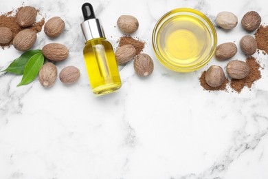 Bottle and bowl of nutmeg oil, nuts on white marble table, flat lay. Space for text