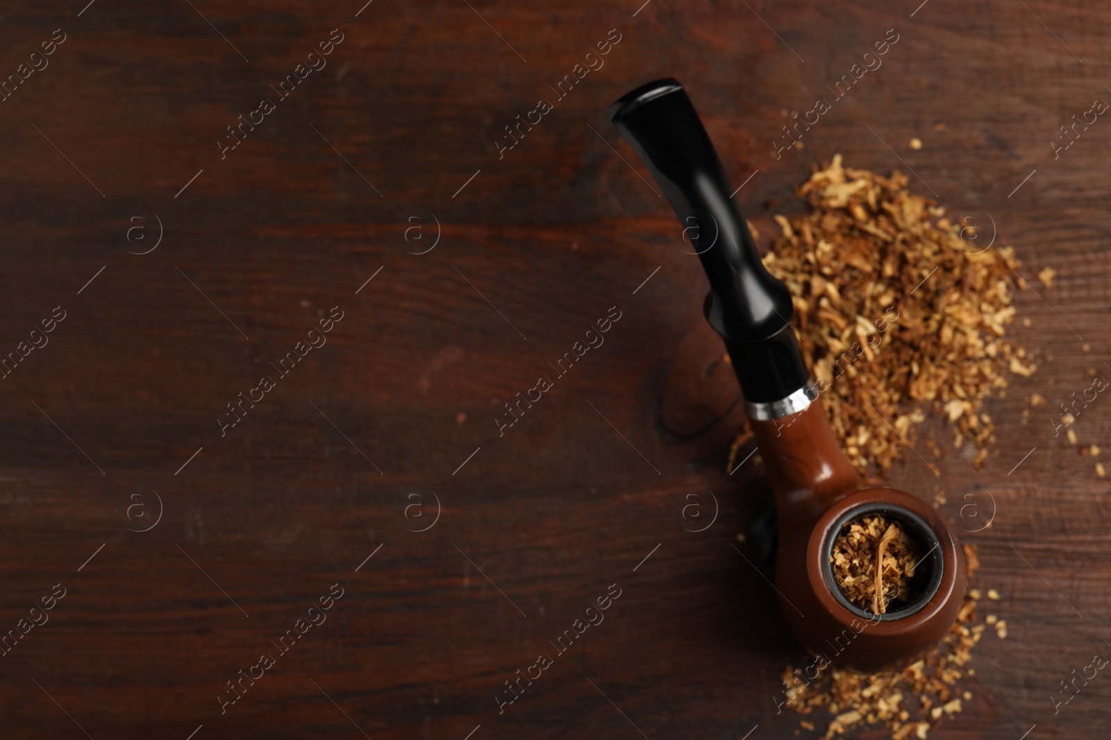 Photo of Smoking pipe with tobacco on wooden table, above view. Space for text